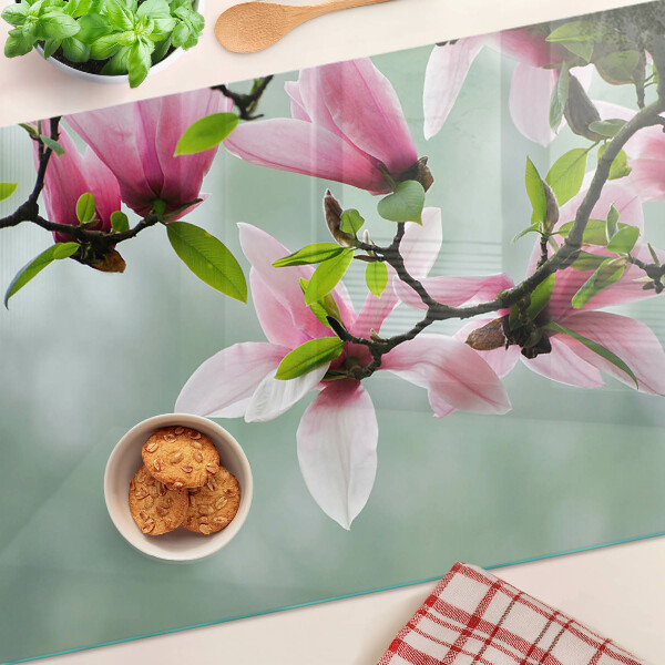 Tabla de cortar de cristal Flores de magnolia sobre un fondo verde.