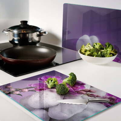 Tabla de cortar Flores de orquídea sobre un fondo de piedras.