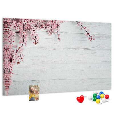 Tablero de corcho decorado con diseño de ramas florales sobre fondo de madera blanca
