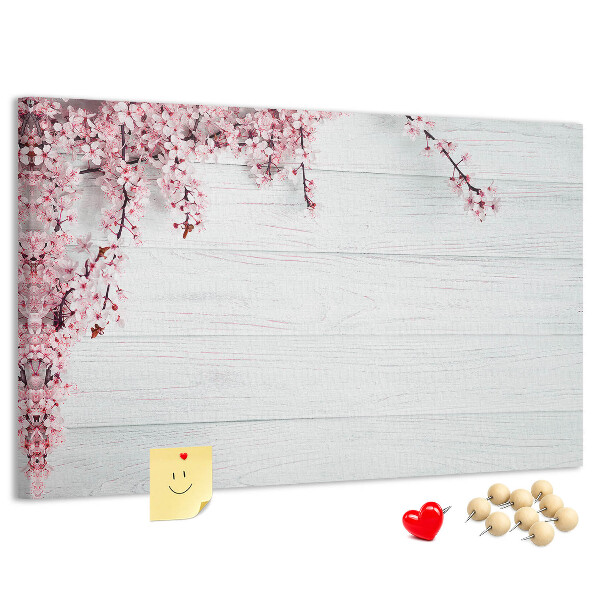Tablero de corcho decorado con diseño de ramas florales sobre fondo de madera blanca
