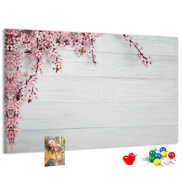 Tablero de corcho decorado con diseño de ramas florales sobre fondo de madera blanca
