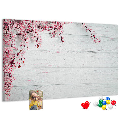 Tablero de corcho decorado con diseño de ramas florales sobre fondo de madera blanca