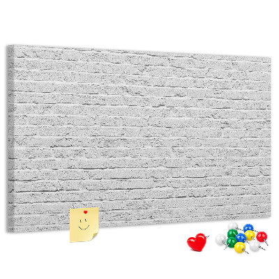 Tablero de anuncios Pared de ladrillo blanco con chinchetas de colores.