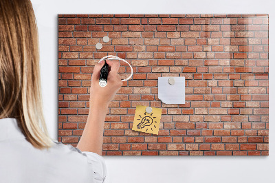 Pizarra borrable de cristal con imanes Un tablero de notas en una pared de ladrillos.