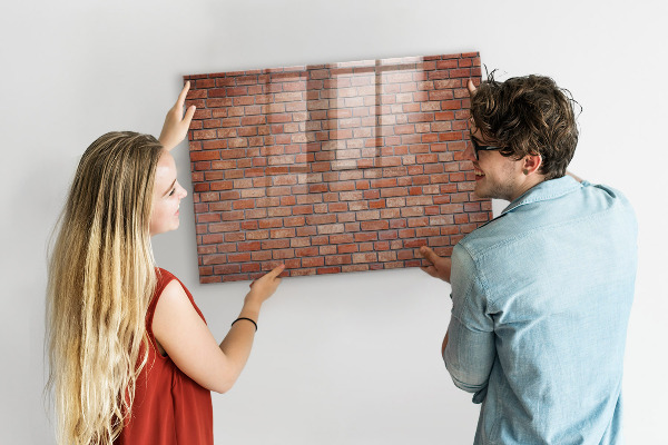 Pizarra borrable de cristal con imanes Un tablero de notas en una pared de ladrillos.