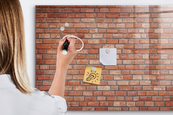 Pizarra borrable de cristal con imanes Un tablero de notas en una pared de ladrillos.