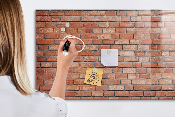 Pizarra borrable de cristal con imanes Un tablero de notas en una pared de ladrillos.