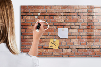 Pizarra borrable de cristal con imanes Un tablero de notas en una pared de ladrillos.