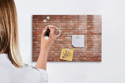 Pizarra borrable de cristal con imanes Un tablero de notas en una pared de ladrillos.